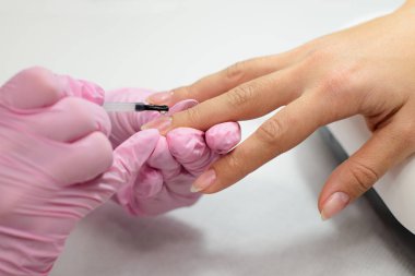 Salon ortamında küçük fırça kullanan kadınlardan manikür tedavisi alan closeup kadın elleri, pembe havlu yüzeyi, bulanık arka plan ürünleri.