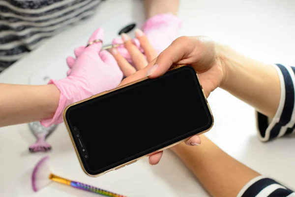 Metin için boş cep telefonu ekranı. Bir kadın cep telefonu kullanarak, bir güzellik tarafından manikür ve tırnak bakımı için bir prosedür alıyor. Bir kadın bir güzellik salonunda çivi, manikür alır.