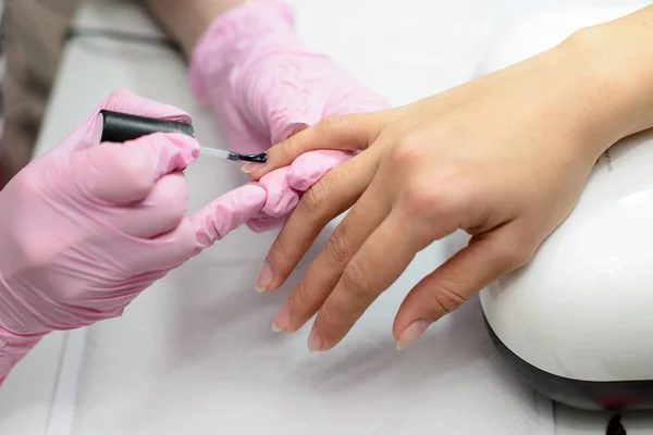 Nahaufnahme Frauen Hände bekommen Maniküre Behandlung von Frau mit kleinen Pinsel in Salonumgebung, rosa Handtuchoberfläche, verschwommenen Hintergrund Produkte. — Stockfoto