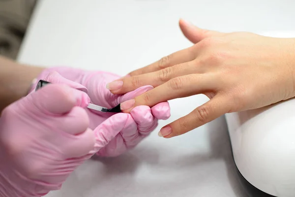 Nahaufnahme Frauen Hände bekommen Maniküre Behandlung von Frau mit kleinen Pinsel in Salonumgebung, rosa Handtuchoberfläche, verschwommenen Hintergrund Produkte. — Stockfoto