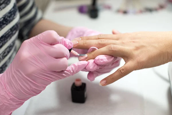 Primeros planos de las manos de las mujeres que reciben tratamiento de manicura de la mujer usando un cepillo pequeño en el ambiente del salón, superficie de la toalla rosa, productos de fondo borroso . —  Fotos de Stock