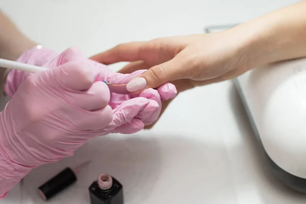 Nahaufnahme Frauen Hände bekommen Maniküre Behandlung von Frau mit kleinen Pinsel in Salonumgebung, rosa Handtuchoberfläche, verschwommenen Hintergrund Produkte. — Stockfoto