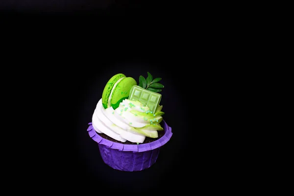 Cupcake mit Schlagsahne, Schokoriegel, dekorierte Makronen auf schwarzem Hintergrund. Bild für ein Menü oder einen Süßwarenkatalog. mit Platz für Text. — Stockfoto
