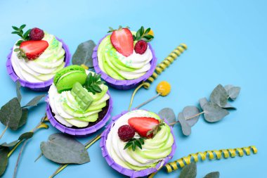 Krem şantili kekler çikolatalı gofret, çilek, mavi arka planda badem kurabiyesi. Menü ya da şekerleme kataloğu için resim. Metin için yeri var. okaliptüs yapraklarıyla süslenmiş..