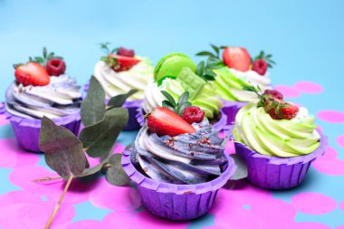 Krem şantili kekler çikolatalı gofret, çilek, mavi arka planda badem kurabiyesi. Menü ya da şekerleme kataloğu için resim. Metin için yeri var. Pembe konfetilerle süslenmiş..