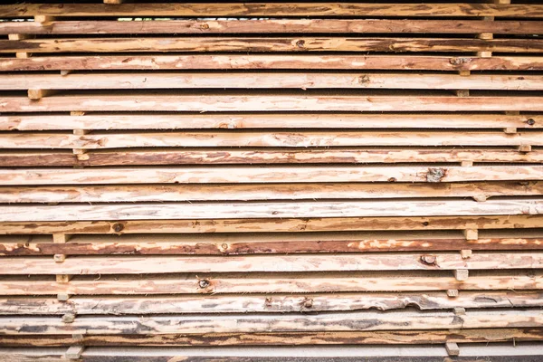 Folded in wooden piled beige beech boards. Background of uneven bars in sawmill