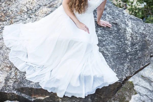 Bride in white dress on large stone. Place for text near beautiful girl in dress