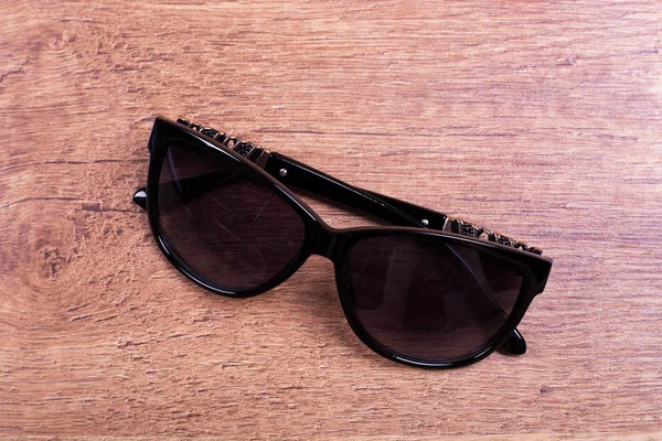 Black frame sunglasses on wood floor. Women\'s sunglasses on laminate
