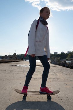 Güneşli bir günde iskelede kaykay süren bir kız..