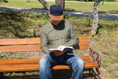 .Adam yazın bankta kitap okur..