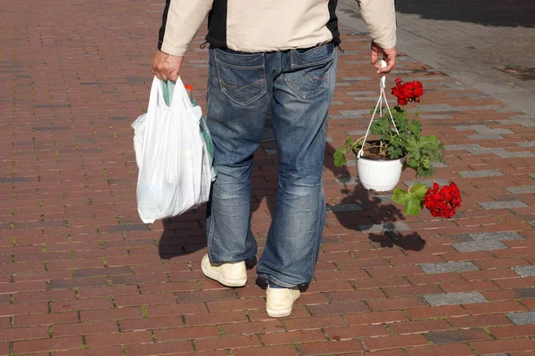 男は花の鍋に花と包装で通りを歩く — ストック写真