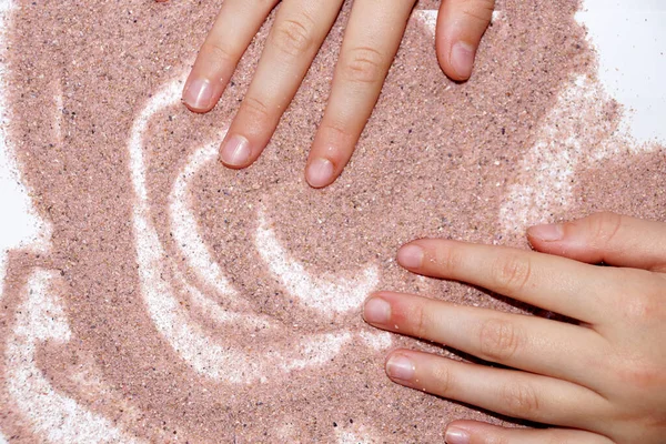 sand therapy, two hands draw with pink sand on a white table.