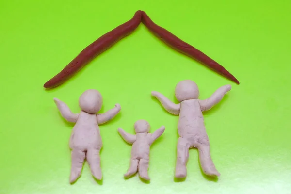 Bir erkek, bir kadın ve bir çocuğun neşeli figürleri, yeşil arka planda, evinin çatısının altında aileyi sembolize ediyor.