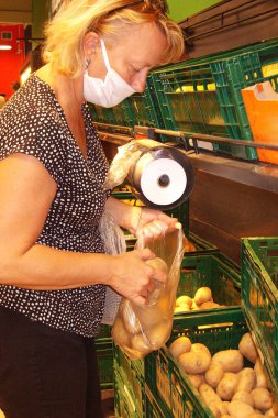 Maskeli bir kadın süpermarkette torbaya patates koyar.