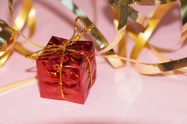 shiny red gift box and gold ribbon on pink background close up