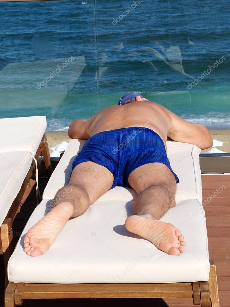a man sunbathes on a sun lounger on a sun terrace overlooking the sea.