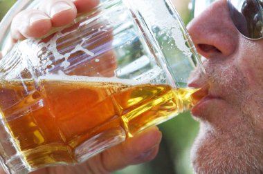 Adam doğadaki büyük cam bardaktan bira içiyor, yakın plan.