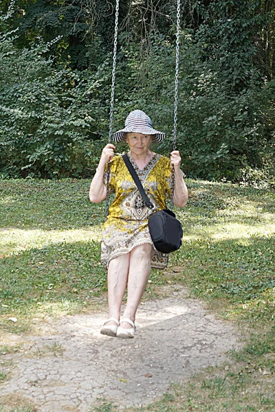 夏の公園でブランコに乗っているお年寄りの女性は — ストック写真