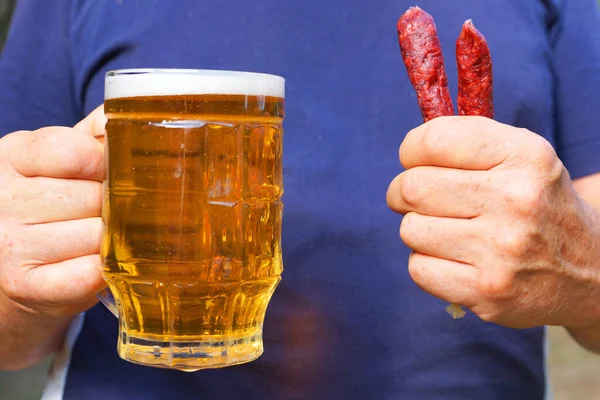 a mug with beer and sausages in the hands of a man close up
