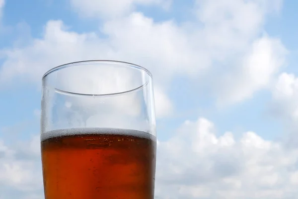glass with beer on the background of a light cloudy sky, copy space