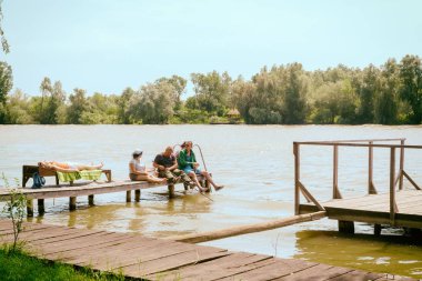 Vilkovo, Ukrayna - Mayıs, 26, 2018: Bir grup insanlar dinlenme ve nehir kıyısında ahşap bir iskele balık.