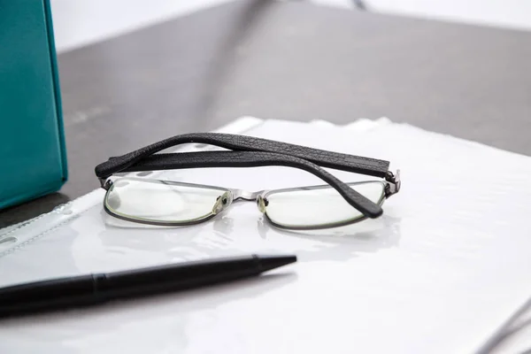 Black-rimmed optical glasses and black pen on documents on grey marble background