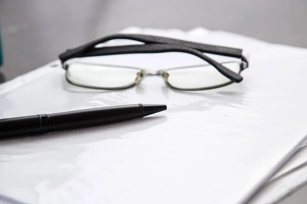 Black-rimmed optical glasses and black pen on documents on grey marble background