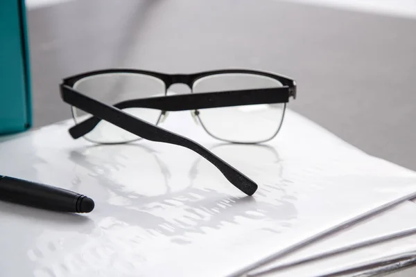 Black-rimmed optical glasses and black pen on documents on grey marble background