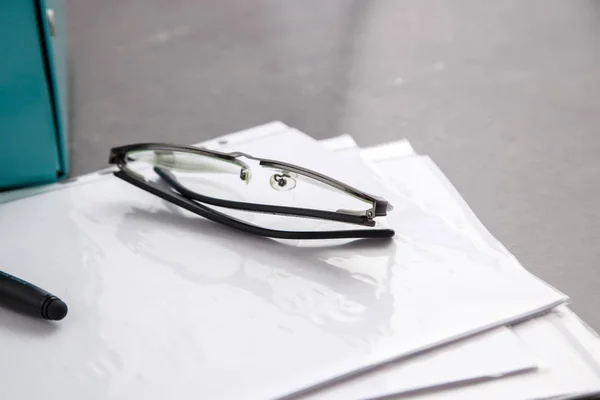 Black-rimmed optical glasses and black pen on documents on grey marble background