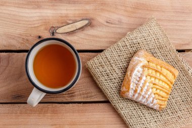 Çay bir fincan ve ahşap bir masa üzerinde bir tuval üzerine süzme peynir ile bir pasta
