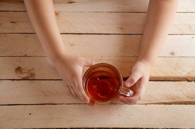 Çocuk bir içkiyle şeffaf Kupası bir ahşap antika arka plan üzerinde eller. Yukarıdan görüntülemek