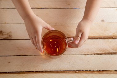 Çocuk bir içkiyle şeffaf Kupası bir ahşap antika arka plan üzerinde eller. Yukarıdan görüntülemek