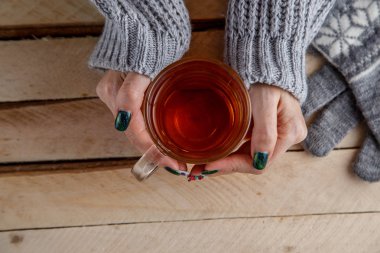 Kadınların elleri şeffaf bir bardak çay tutan bir gri süveterli. Yukarıdan görüntüleyin. Işık vintage ahşap arka plan üzerinde.