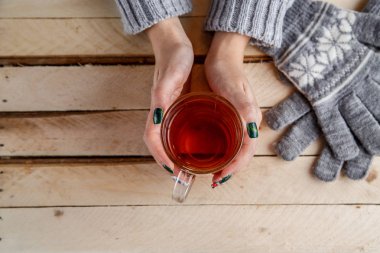 Kadınların elleri şeffaf bir bardak çay tutan bir gri süveterli. Yukarıdan görüntüleyin. Işık vintage ahşap arka plan üzerinde.