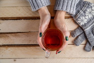 Kadınların elleri şeffaf bir bardak çay tutan bir gri süveterli. Yukarıdan görüntüleyin. Işık vintage ahşap arka plan üzerinde.