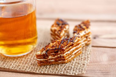 Dilim kek katmanları ile bir bardak çay ahşap bir masa üzerinde krem ile