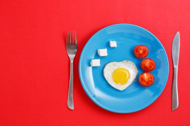 Kavramı için aşk hikayeleri ve Sevgililer günü için. Kızarmış yumurta, peynir ve domates ile mavi bir plaka üzerinde bir kalp şeklinde.