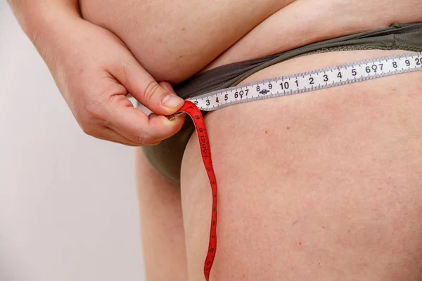 a middle-aged woman with overweight in underwear measuring her body