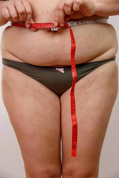 a middle-aged woman with overweight in underwear measuring her body