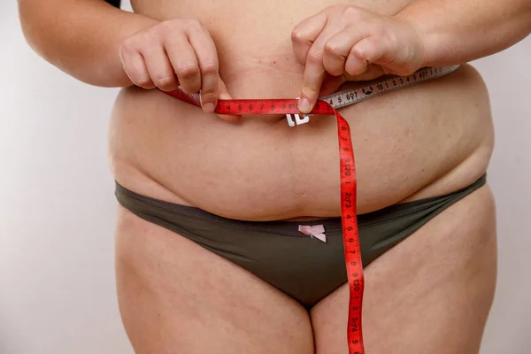 a middle-aged woman with overweight in underwear measuring her body