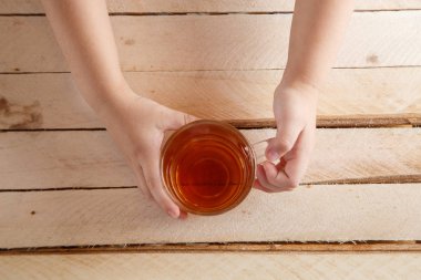 hafif ahşap bir arka plan üzerinde çay şeffaf bir bardak tutan çocuğun elleri