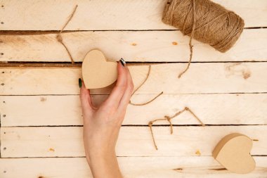 women's hands spread hearts and the word love of threads on a light wooden background. the view from the top