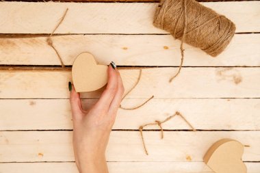 women's hands spread hearts and the word love of threads on a light wooden background. the view from the top