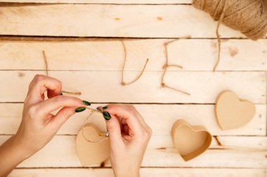 women's hands spread hearts and the word love of threads on a light wooden background. the view from the top
