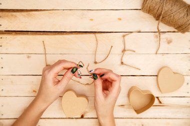 women's hands spread hearts and the word love of threads on a light wooden background. the view from the top