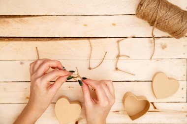 women's hands spread hearts and the word love of threads on a light wooden background. the view from the top