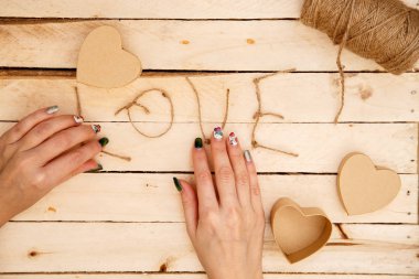 women's hands spread hearts and the word love of threads on a light wooden background. the view from the top