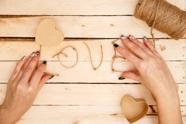 women's hands spread hearts and the word love of threads on a light wooden background. the view from the top