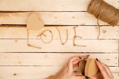 women's hands spread hearts and the word love of threads on a light wooden background. the view from the top