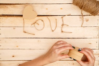 women's hands spread hearts and the word love of threads on a light wooden background. the view from the top